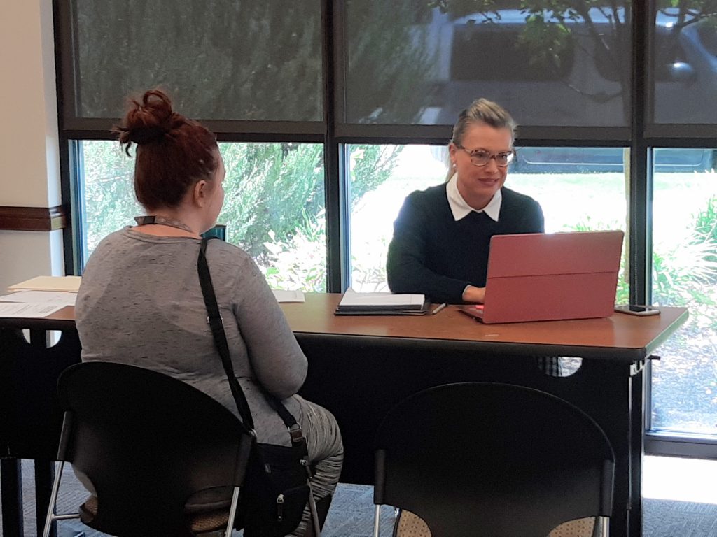 Lawyer at table with laptop and woman sitting in chair.